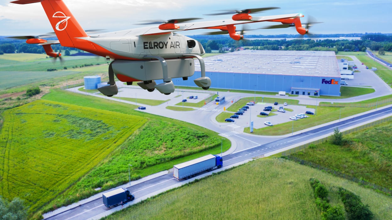 An orange plane flying above a green field, highway, and FedEx building 