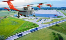 An orange plane flying above a green field, highway, and FedEx building 