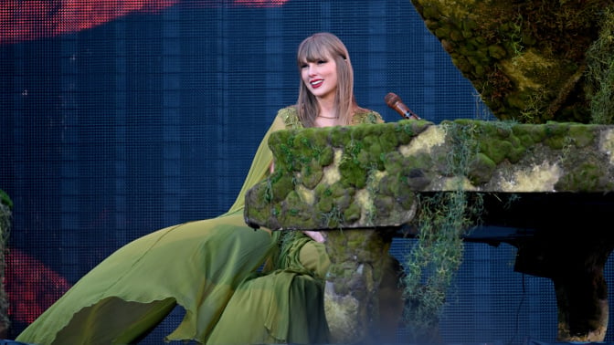 Taylor Swift sitting at a piano in a green dress. 