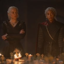 Rhaenyra and Baela Targaryen stand at the head of a war table covered in candles.