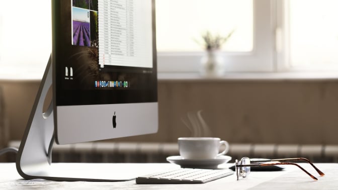 iMac computer, steaming coffeem and glasses on a home desk.