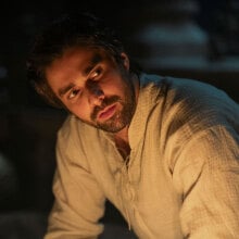 A man sits in a dark room, looking serious.