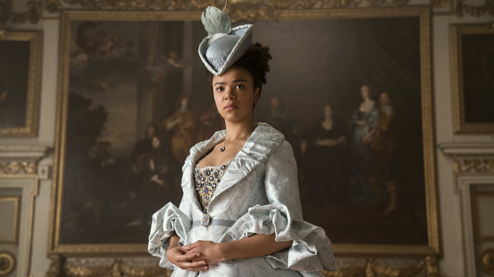 A woman in formal Regency attire stands in front of a painting.