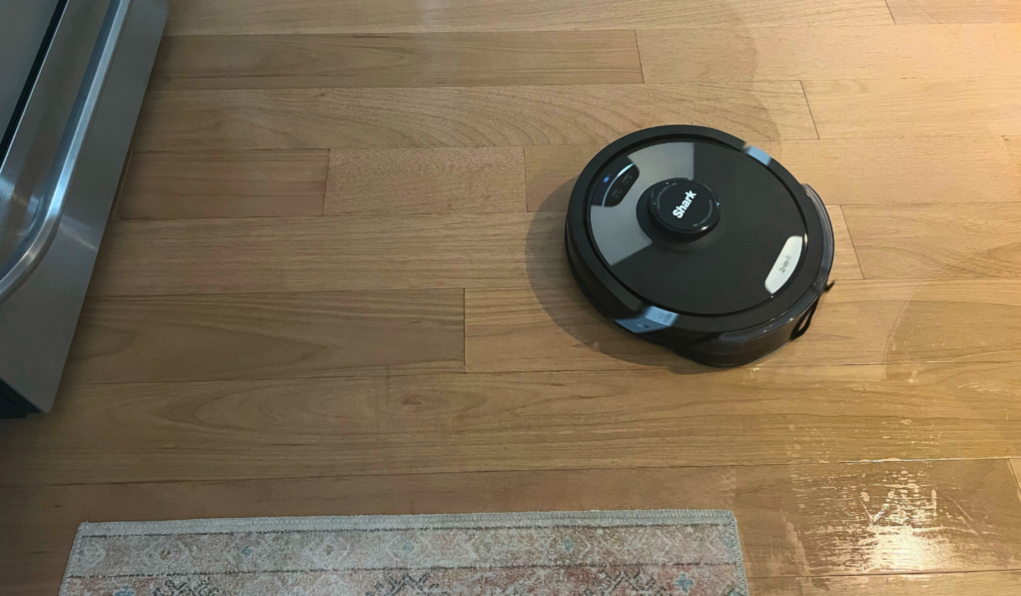 Shark Matrix Plus robot vacuum mopping hardwood floor with stove and rug in peripherals