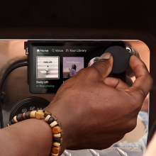 A hand turning a dial on a small Car Thing screen.