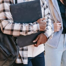 Bodies of two people, one carrying a laptop and a backpack