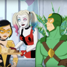 A screenshot from 'Kite Man: Hell Yeah!' showing Harley Quinn offering a cheese plate to Golden Glider as Kite Man sits beside her.