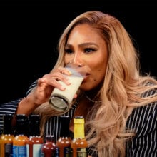 A woman sits at a table covered in sauce bottles, drinking a glass of milk.