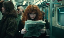 A woman with voluminous, curly red hair reading a newspaper on a public train; still from "Russian Doll" Season 2.