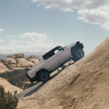 A white Hummer EV climbs up a steep desert hill.