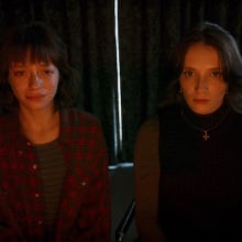 Two women sitting side by side in a dim room under red light.