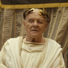 A man dressed in a white robe with a gold crown, like a Roman emperor.