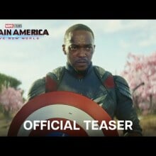 Sam Wilson holds the Captain America shield while standing in front of a group of cherry blossom trees.