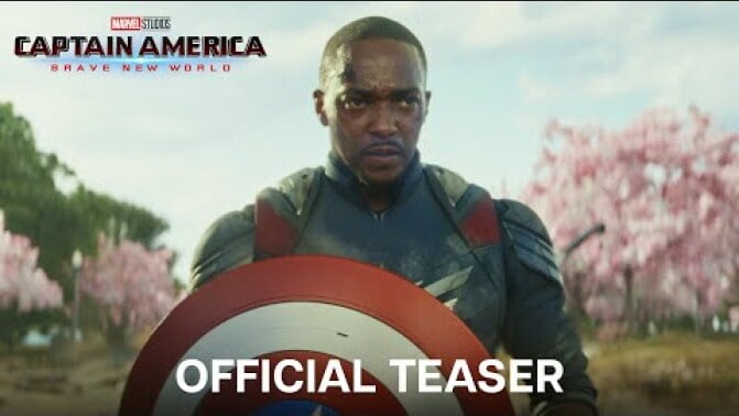 Sam Wilson holds the Captain America shield while standing in front of a group of cherry blossom trees.