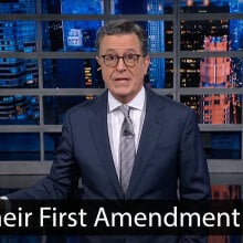 A man in a suit stands on a stage. A quote at the bottom reads "It's their First Amendment right."