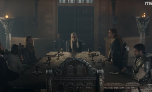 A group of people in medieval clothes sit around a large table in a gloomy room.