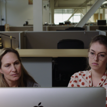 Two women stare at a computer screen while sitting in an office. 