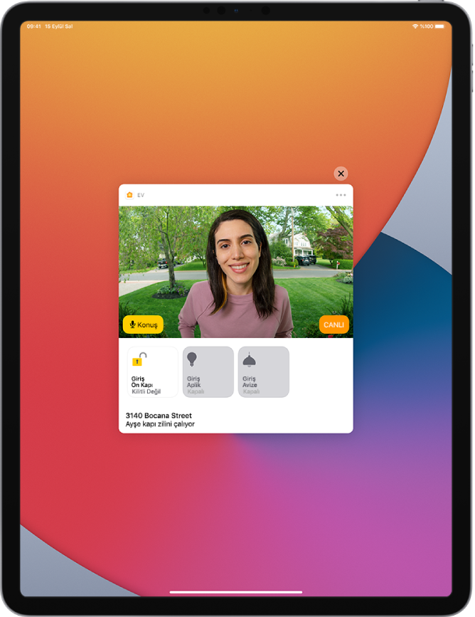 iPad ekranında Ev uygulamasından bir bildirim. Sol tarafta bir Konuş düğmesiyle ön kapıdaki bir kişinin resmi gösteriliyor. Alt tarafta ön kapı ve giriş ışıkları için aksesuar düğmeleri var. Aksesuar düğmelerinin alt tarafında “Ayşe kapı zilini çalıyor” sözcükleriyle birlikte ev adresi görünüyor. Bildirimin sağ üst tarafında Kapat düğmesi var.