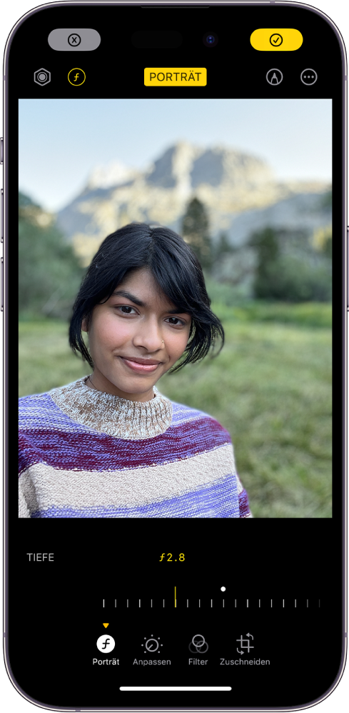 Der Bildschirm „Bearbeiten“ für ein Porträt in der App „Fotos“. Ein Porträt wird in der Bildschirmmitte angezeigt. Darunter ist ein Schieberegler zum Einstellen der Tiefeneffektanpassung zu sehen. Unter dem Schieberegler werden von links nach rechts die Tasten „Porträt“, „Anpassen“, „Filter“ und „Zuschneiden“ angezeigt. Die Taste „Porträt“ ist ausgewählt.