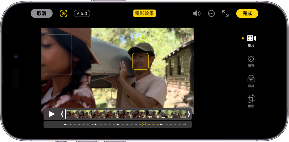 橫向的「電影效果」模式影片之「編輯」畫面。畫面左上方是「取消」按鈕，「電影效果」「手動」按鈕，以及「景深調整」按鈕。在畫面頂部中間，「電影效果」按鈕已被選取。畫面右上方是「音量」按鈕、「更多選項」按鈕、「進入全螢幕」按鈕，以及「完成」按鈕。影片位於畫面中間，在焦點主體的周圍有一個方框。影片下方是影格顯示器，顯示影片中主體焦點更改的點。編輯按鈕位於畫面的右側，由上至下為：「影片」、「調教顏色」、「濾鏡」和「裁剪」。