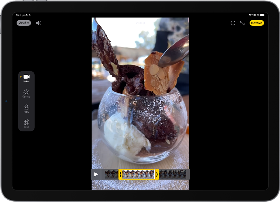 Na obrazovce Úpravy v aplikaci Fotky se uprostřed přehrává video. Pod videem se zobrazuje prohlížeč snímků videa se žlutým rámečkem vyznačujícím snímky, které budou zahrnuty do zkráceného videa. Na levé straně obrazovky jsou vidět tlačítka Video, Úpravy, Filtry a Ořez. Tlačítko Video je vybrané.