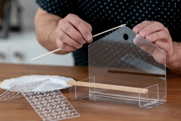 Use a wooden skewer to apply a thin coat of waterproof super glue to the roof and sides of the tray and glue together. Then, make a perch by adding a wooden dowel to the edge of the tray using waterproof super glue. Let dry for 24 hours. Tip: Use painter’s tape and a scrap piece of cardboard to hold the bird feeder in place as it dries.