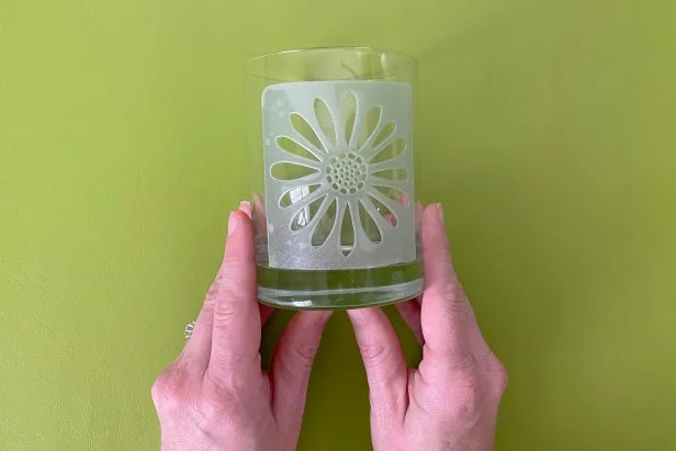 Place the adhesive flower stencil onto one side of the glass close to the center. Press firmly on the stencil to ensure no gaps. Next, put on protective gloves. Using a paint brush, brush a thick layer of etching cream over the stencil on the glass and let it sit for about 3 minutes. Then, thoroughly rinse the glass and stencil with water. Remove stencil from glass and continue rinsing with water until all etching cream is removed. Repeat above steps on the other side of the glass if desired.