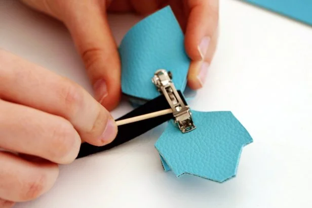 Add hot glue to the end of the black rectangle. Glue the rectangle so it covers the bottom of the hair clip. Use a toothpick to help press it into place. Let dry.Add more glue to the center of the bow and wrap the rectangle around. Let dry. Add glue to the next section of the rectangle and feed it back under the hair clip, pulling it tight and pressing it into place with a toothpick. Trim the excess fabric.