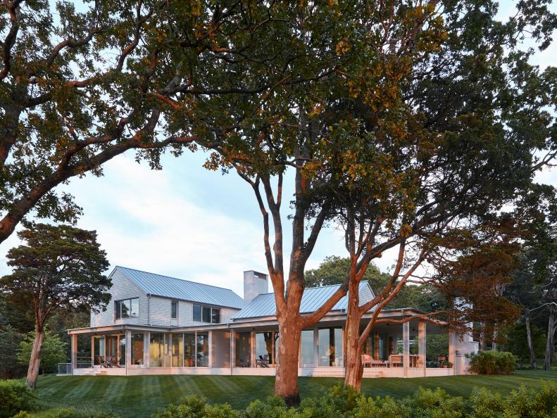 Family home with pillared covered wraparound patio and sloped lawn.