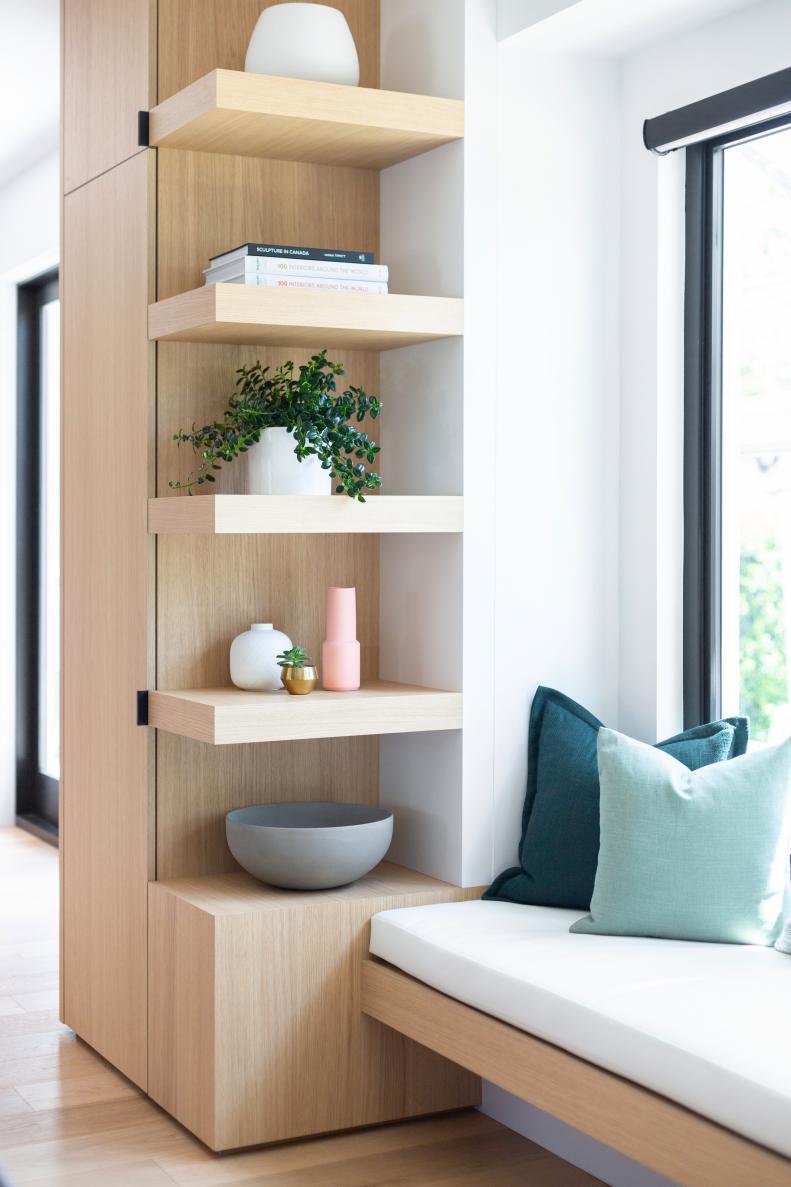 Open shelving next to a sunny window seat with green pillows