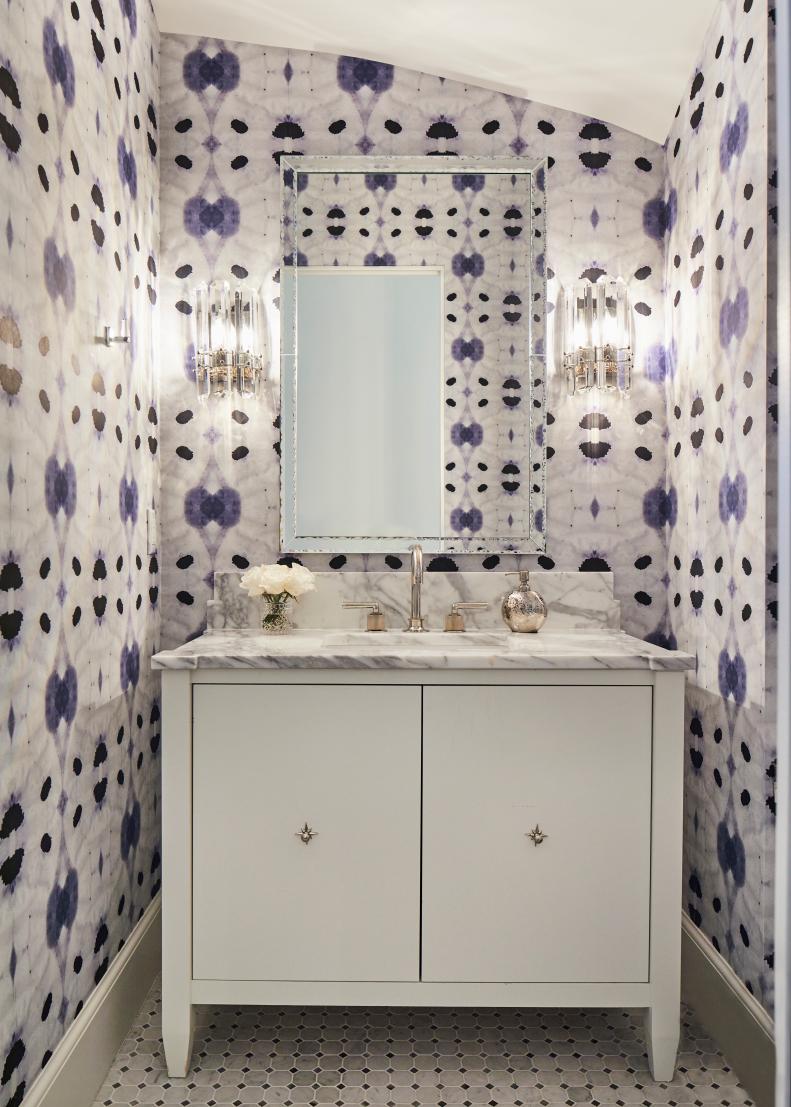 A sink and mirror in a small bathroom with purple printed wallpaper