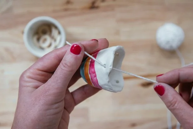 Use cotton twine and small wooden rings to hang the pot (Image 1). Thread twine through the first hole and then through the wooden ring (Image 2). Then, thread through the second hole and back through the wooden ring (Image 3). Repeat again with the third hole and tie off to the beginning of the twine (Image 4).