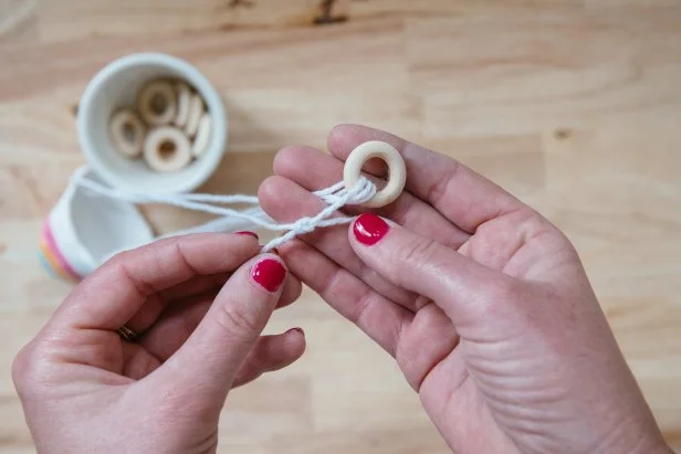 Use cotton twine and small wooden rings to hang the pot (Image 1).Thread twine through the first hole and then through the wooden ring (Image 2). Then, thread through the second hole and back through the wooden ring (Image 3). Repeat again with the third hole and tie off to the beginning of the twine (Image 4).