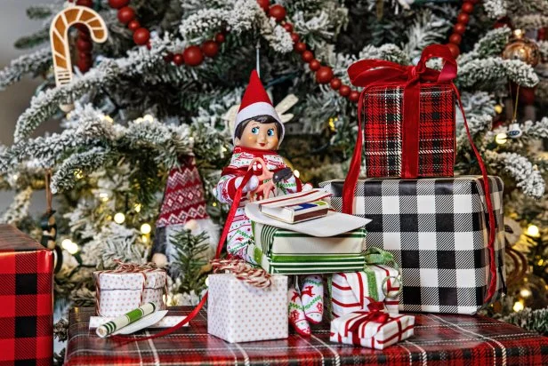 A toy elf poses with several small, wrapped Christmas presents.