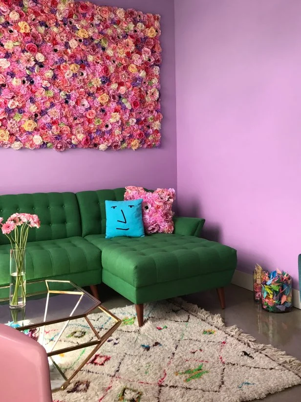 This fun living room from HGTV Magazine features purple-pink walls, a green sofa and a faux flower wall.