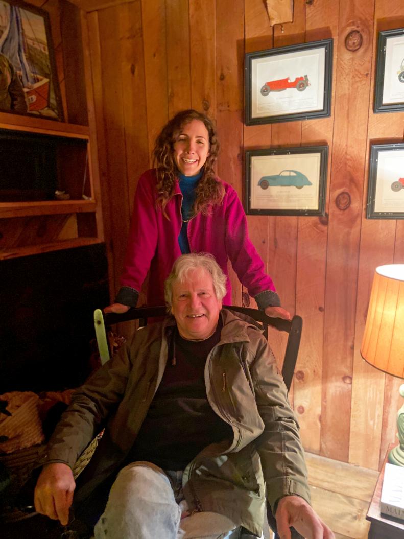 Woman Stands Behind Seated Man in Living Room With Maritime Artwork