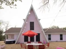 Front of A-Frame Home Flanked by Bistro Lights With Patio Furniture in Front