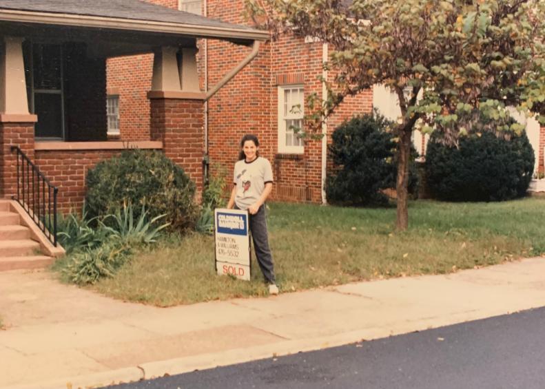 Woman stands in yard beside a sold sign in vintage photo