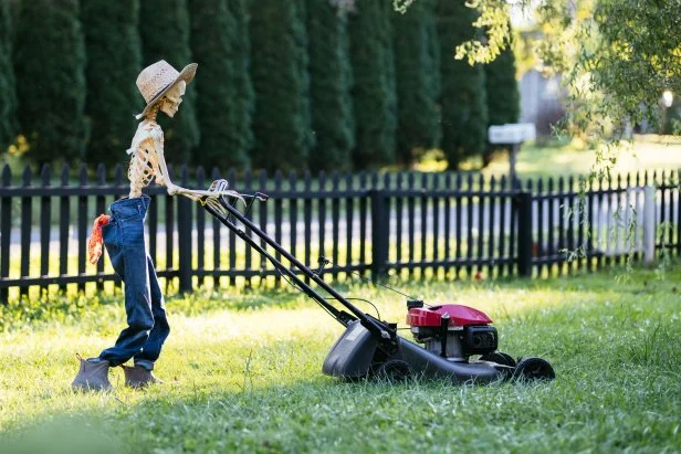 Life-sized skeleton wearing jeans and mowing a yard