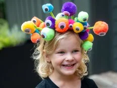 Girl wearing a colorful headband covered with pom-poms and google eyes.