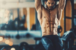 closeup front view of a handsome mid 20's man doing abs in a gym he's doing leg raises, shirtless blurry gym equipment in background