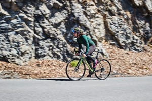 a man riding a bicycle on a road near a rocky cliff