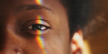 half of a black womans face with a rainbow light reflection over her eye