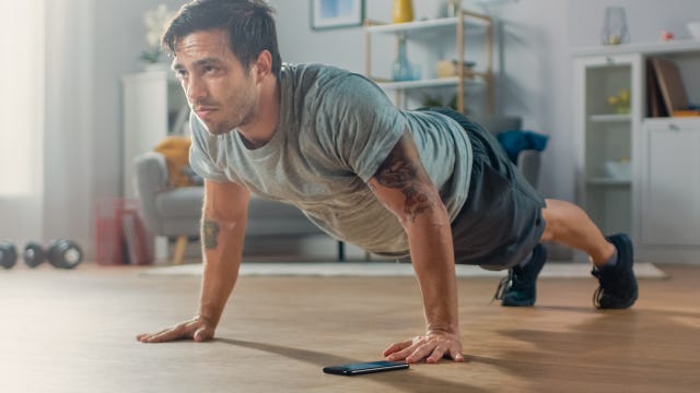 athletic fit man in t shirt and shorts is doing push up exercises while using a stopwatch on his phone he is training at home in his living room with minimalistic interior