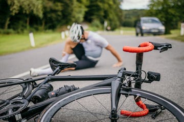 injured cyclist sitting in pain on the road next to the racing bicycle