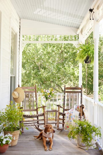 classic white covered farmhouse porch with rocking chairs, dogs, container plants