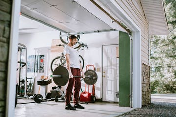 a mid adult man lifts weights in his home garage part of a regular routine, or the new normal with social distancing and covid 19