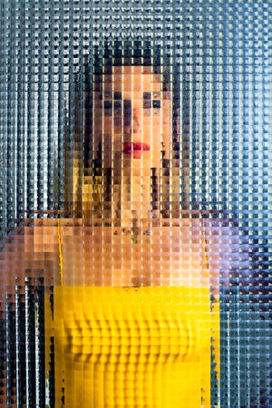 woman in a yellow vest behind distorted glass giving the impression she's been pixelated or censored