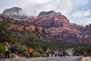 a group of people walking on a road in front of a red rock formation