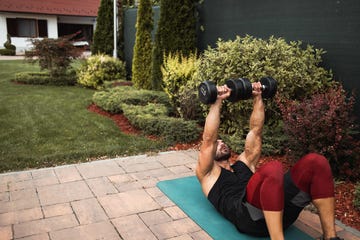 dedicated shirtless muscular caucasian man doing exercises with dumbbel outdoor fitness concept